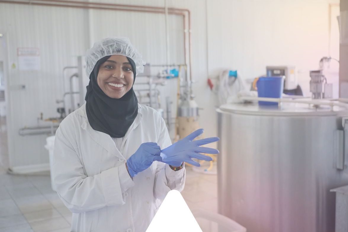 An Environmental Health expert wearing a white safety coat pulls on a blue safety glove as she does some sampling tests for a safety client